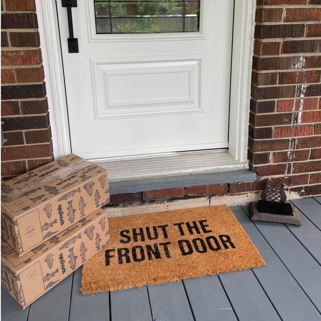 Box of fish on doorstep with mat that says shut the front door