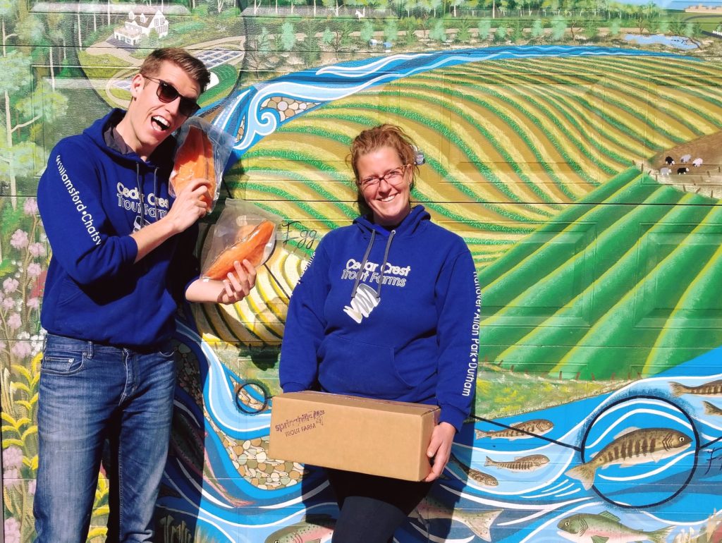 fish farmers holding fish fillets in front of mural